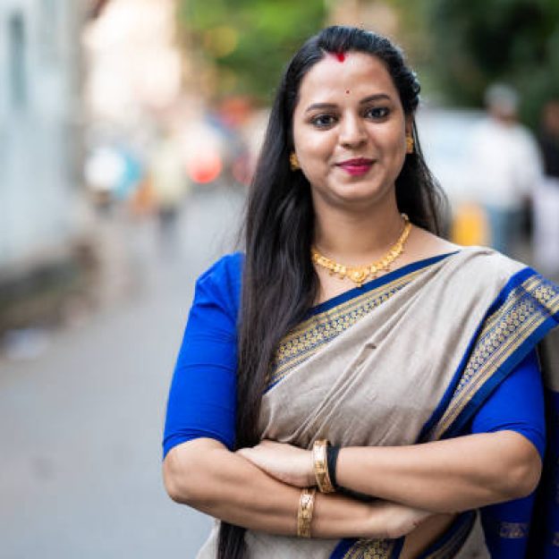 Outdoor waist up portrait of a beautiful Indian woman wearing sari with crossed arms and a smile on her face. She is standing near her car.